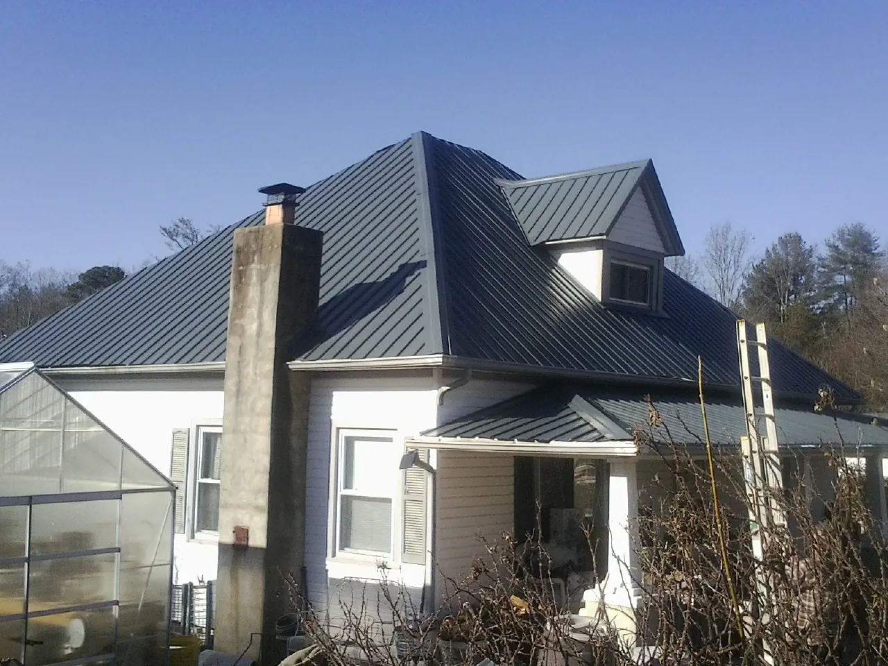 Dark blue standing seam metal roof on a white farmhouse with dormer — Slate & Tile Roof Repair by Roofing Brothers in Ashville